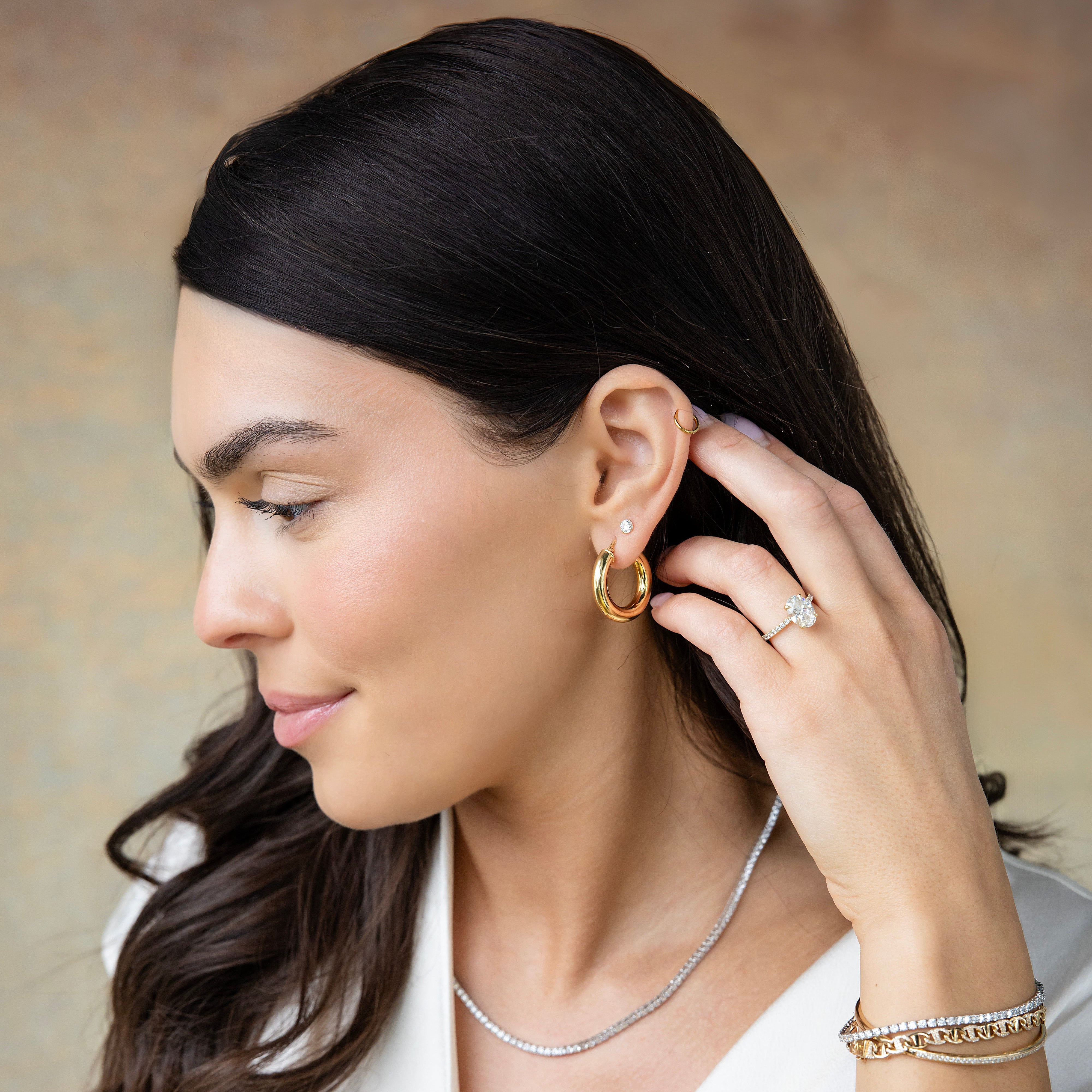 Woman wearing gold earrings, a necklace, and a bracelet against a neutral background